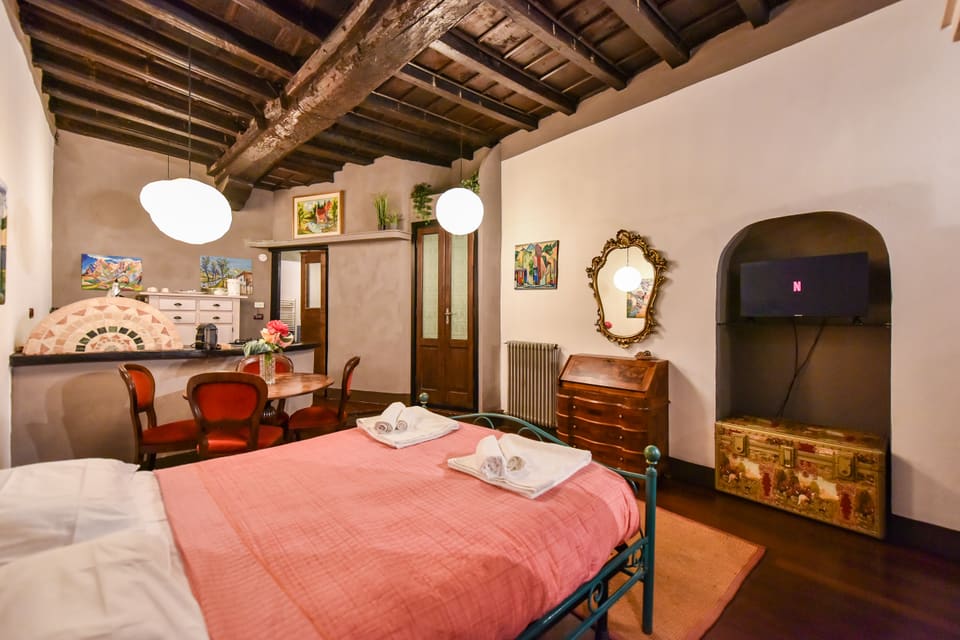 La TV nella nicchia ad arco, il letto e il tavolo da pranzo sotto le travi